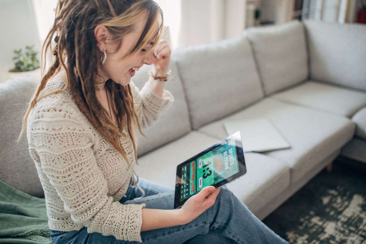 Mulher sentada no sofá usando calça jeans e suéter enquanto joga online no Paripesa Portugal