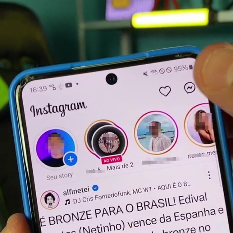 A imagem mostra a tela de um smartphone exibindo o aplicativo Instagram. No topo, há ícones de stories, incluindo um com um anel dourado ao redor, indicando a tendência "gold no Instagram". Abaixo, há uma postagem de um usuário verificado, celebrando uma vitória esportiva do Brasil. A mão de uma pessoa segura o telefone.