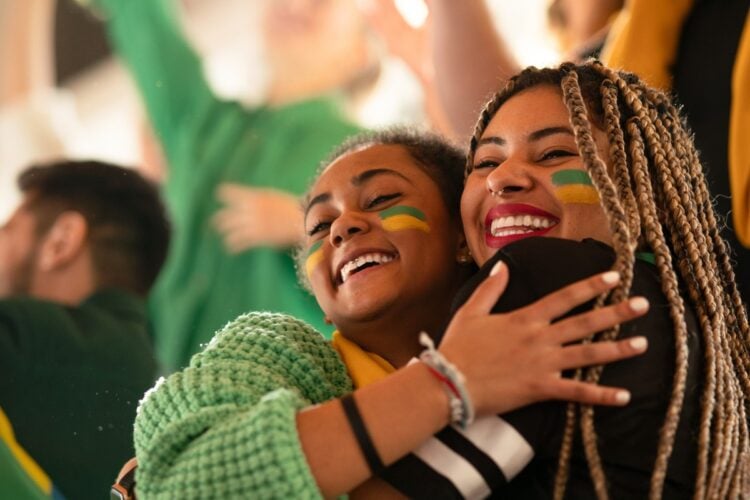 Foto de 2 mulheres abraçadas com o rosto pintado de verde e amarelo. Elas são torcedoras do Brasil nas Olimpíadas 2024. Tudo sobre quando acabam as Olimpíadas 2024