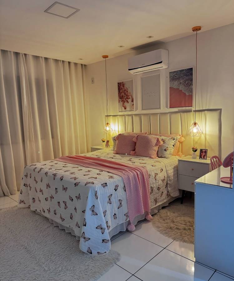 Quarto de casal com cama decorada com colcha de borboletas e almofadas rosa. Luminárias pendentes e cortinas brancas criam um ambiente acolhedor.