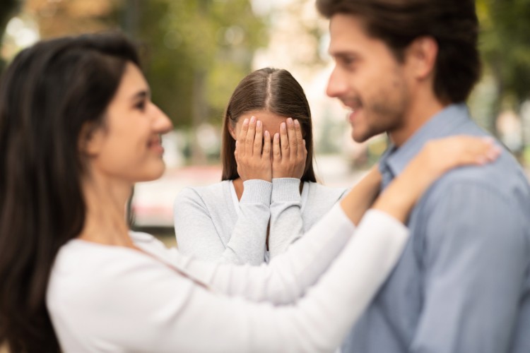 Mulher de pele clara com as mãos no rosto em frente à casal heterossexual de pele clara feliz 