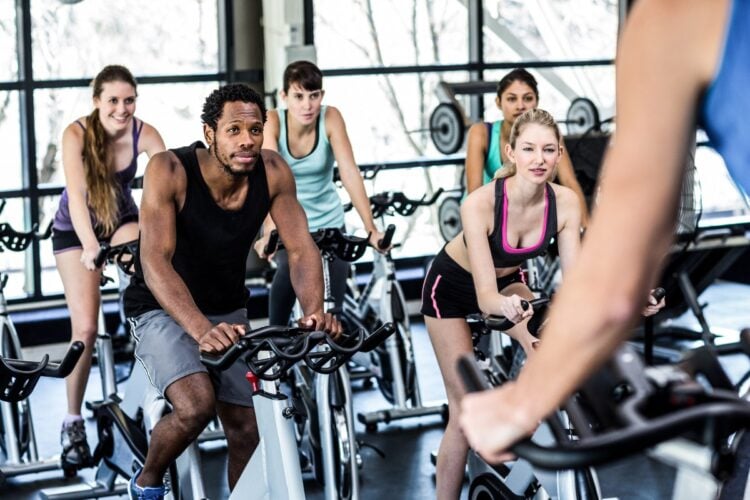 Foto de homem de pele negra e 3 mulheres de pele clara em aula de spinning