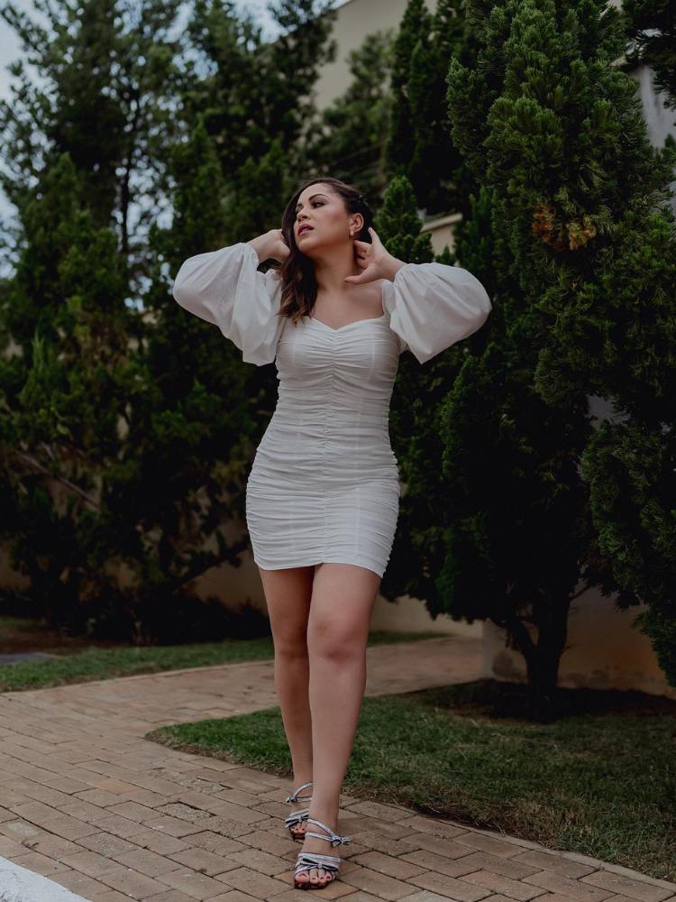 Mulher de pele clara usando vestido curto branco drapeado com mangas bufantes e salto