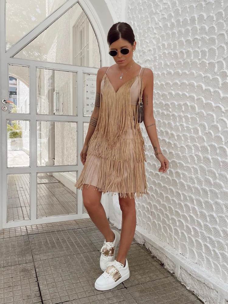 Mulher de pele clara usando vestido dourado com franjas e tênis branco 