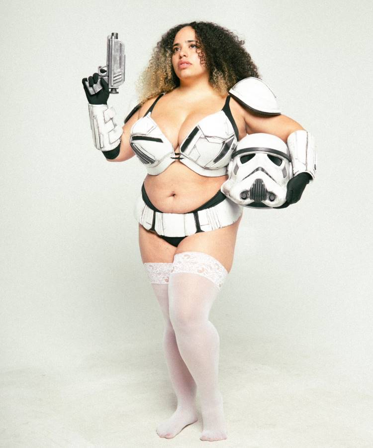 A imagem mostra uma mulher vestida em uma fantasia inspirada em Star Wars, ideal para fantasias femininas para o Halloween. Ela usa uma armadura de stormtrooper estilizada, com peças nos ombros e um capacete na mão. O traje é combinado com meias brancas rendadas e uma pistola futurista, adicionando um toque ousado e criativo. O visual mistura elementos icônicos da saga com um estilo único e moderno, perfeito para se destacar em festas temáticas.