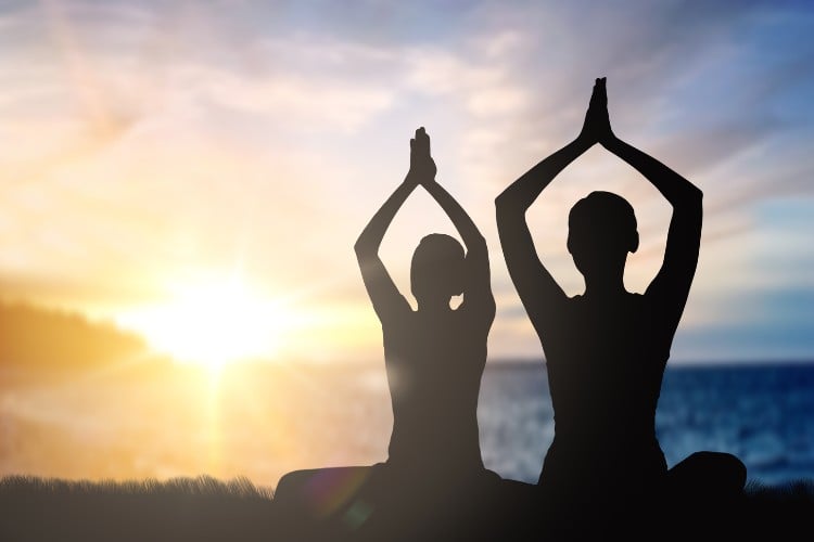 Foto de sombra de duas pessoas meditando no pôr do sol