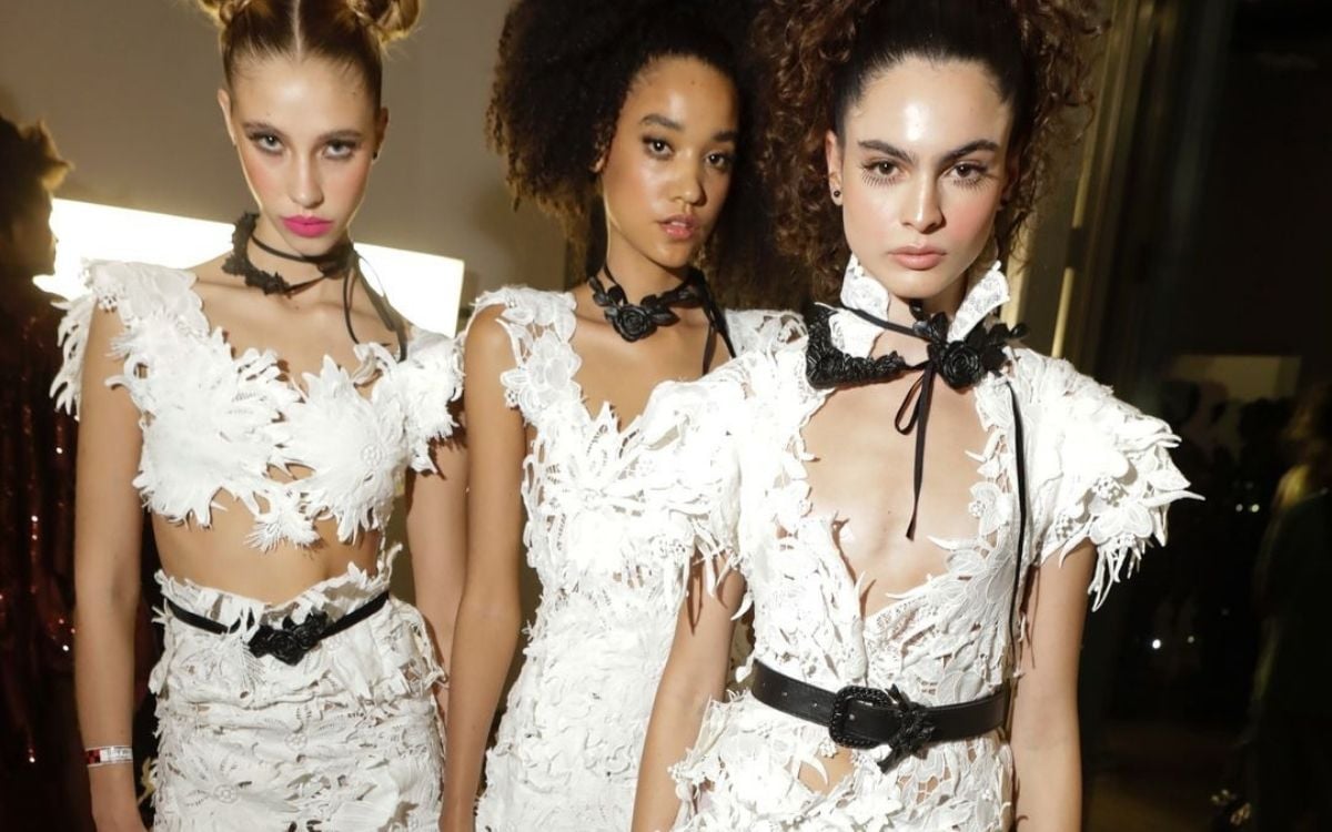 Foto de 3 modelos durante o line-up do SPFW N58 usando vestidos brancos de renda com detalhes em couro preto