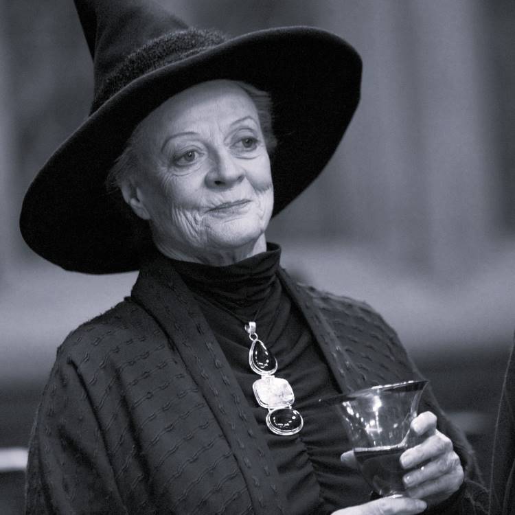 A imagem mostra a atriz de Harry Potter, Maggie Smith, usando um chapéu pontudo, típico de uma bruxa, segurando um copo. A foto está em preto e branco, conferindo um ar clássico e misterioso.