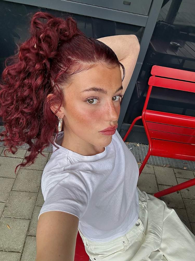 selfie de mlher com cabelo vermelho e roupas brancas, com mão no cabelo 