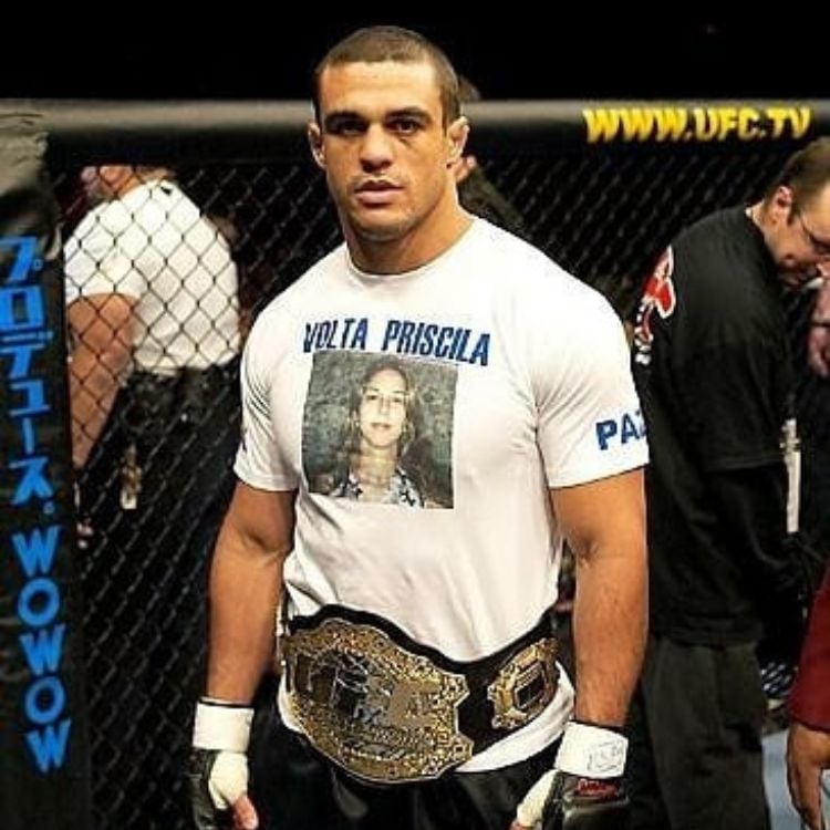 Vitor Belfort usando camiseta branca com foto de Priscila e frase "Volta Priscila", dentro do ringue e usando cinturão 