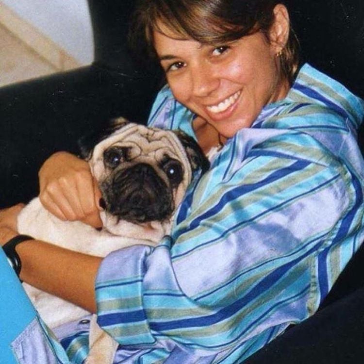 Priscila Belfort usando camisa azul, sentada em sofá preto, segurando um Pug 