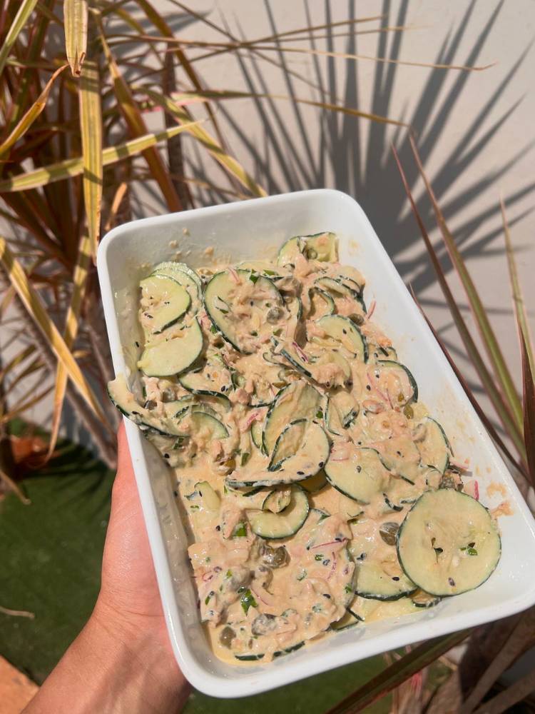 Pessoa de pele clara segurando recipiente branco de louça com salada de pepino cremosa com atum