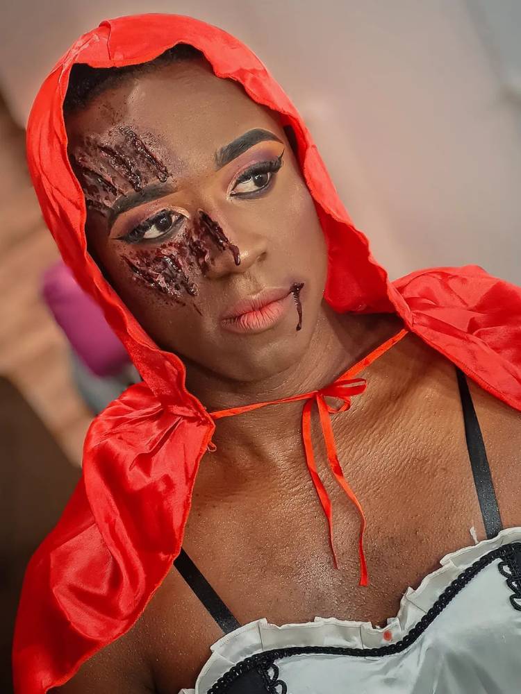 Mulher de pele negra fantasiada de Chapeuzinho Vermelho com arranhão de sangue fake no rosto 