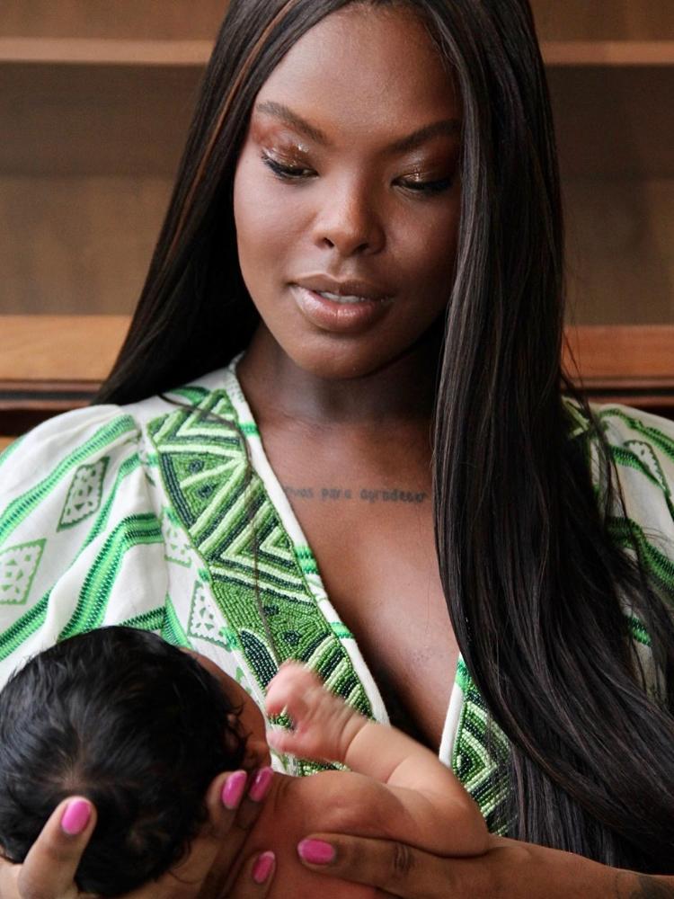 Suelen Gervásio de cabelo liso, usando vestido bege e verde, segurando bebê 