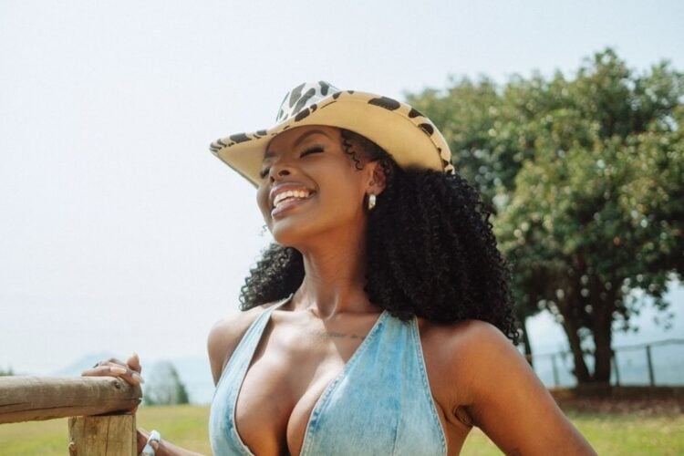 Suelen Gervásio usando chapéu de cowboy e top jeans com paisagem de campo atrás