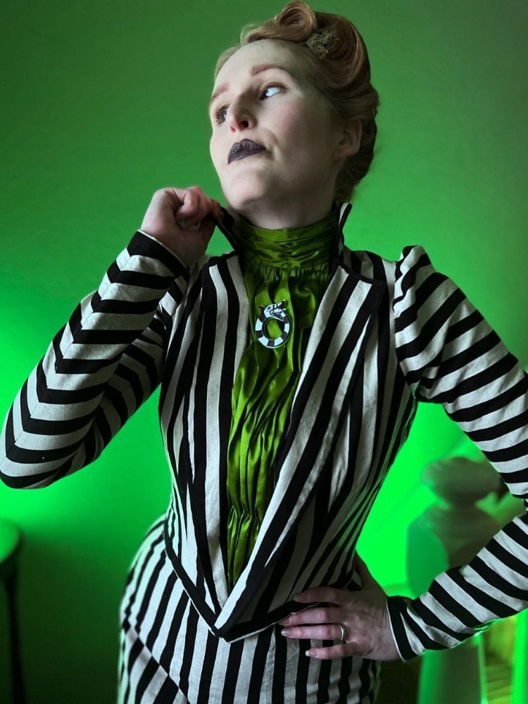 Pessoa fantasiada de Beetlejuice, com camisa verde e terno listado de branco e preto, além de base pálida