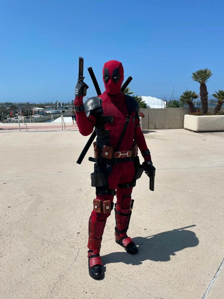 Pessoa fantasiada de Deadpool, com macacão preto e vermelho e armas 