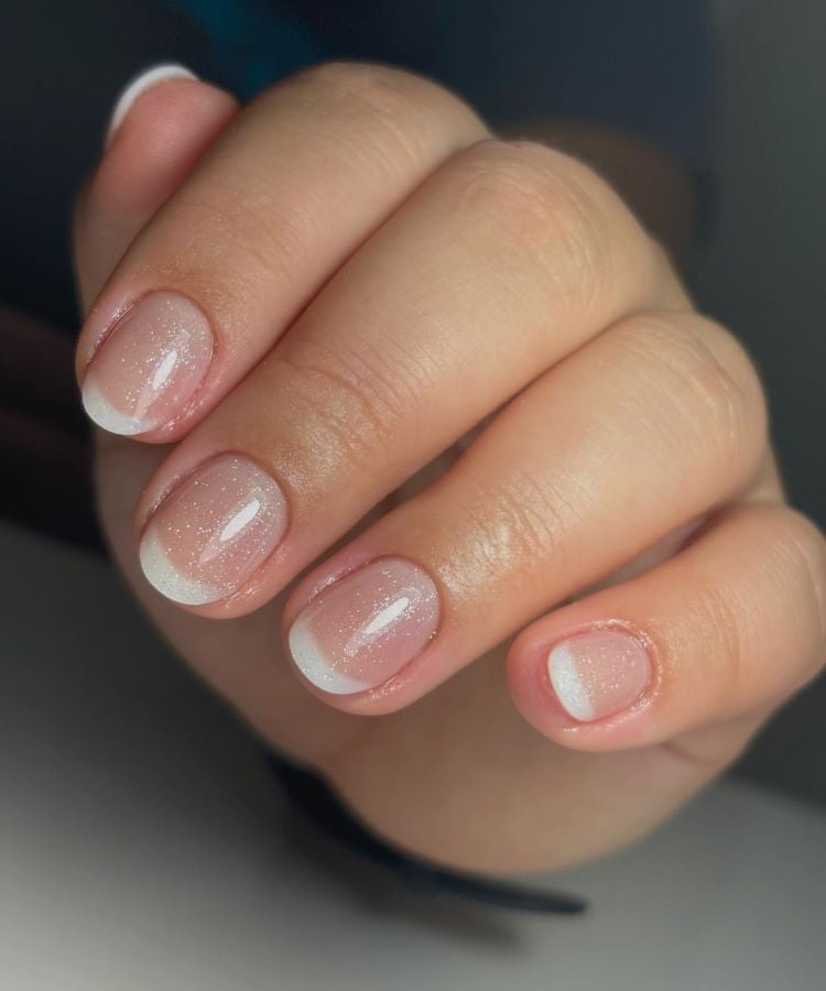 A imagem mostra uma mão com unhas curtas e bem cuidadas, decoradas em um estilo de francesinha. O esmalte é transparente com pontas brancas, criando um visual clássico e elegante. Essa é uma unha decorada simples, ideal para quem prefere um design discreto e sofisticado.