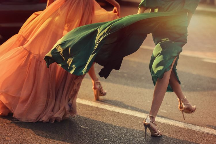 Foto de duas mulheres caminhando pelas ruas de São Paulo: uma usa vestido mullet laranja e outra usa vestido mídi verde