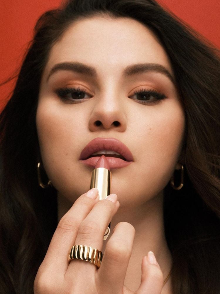 Selena Gomez de maquiagem leve passando batom matte amarronzado