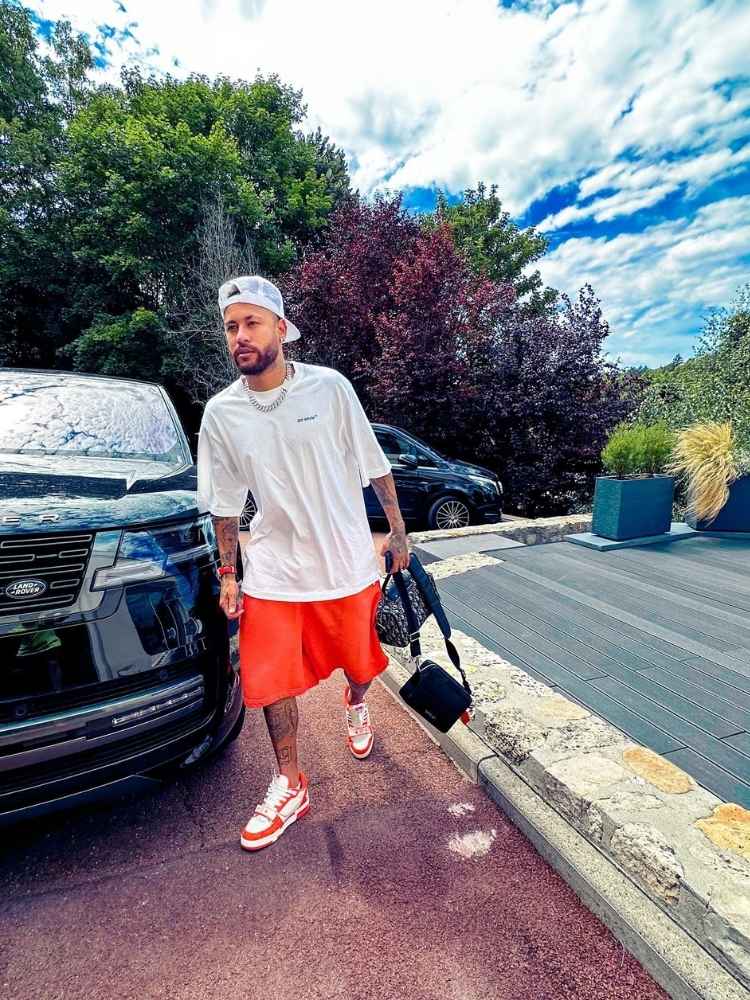 Neymar Jr usando blusa branca e bermuda laranja ao lado de Range Rover First Edition preta 