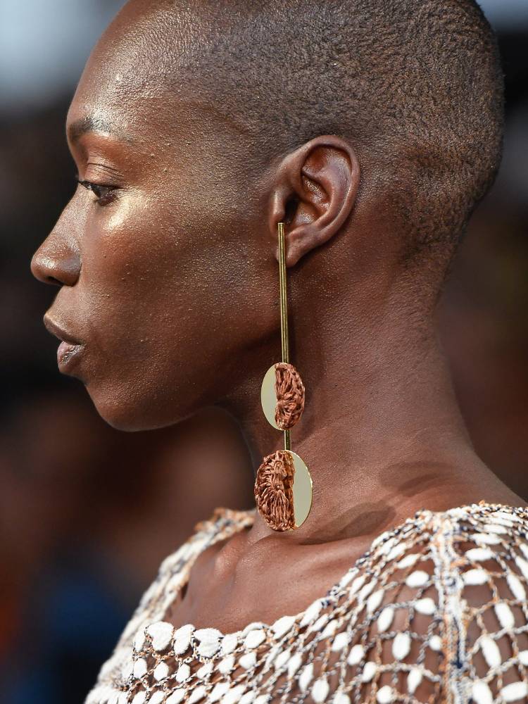 Mulher de pele negra de perfil usando brinco dourado e bege 