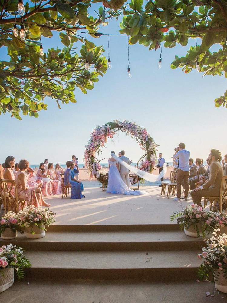 Camila Queiroz e Klebber Toledo de costas para a foto e de frente para o mar de Jericoacoara durante casamento com convidados sentados 