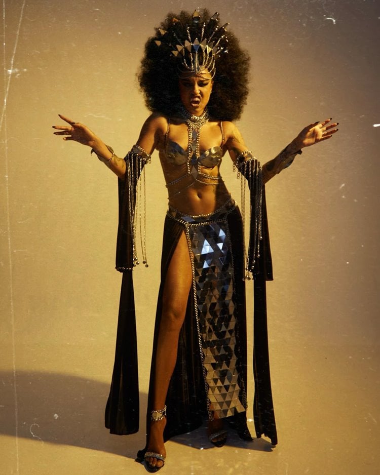 Cris Paladinho está vestida como Akasha, a vilã de "A Rainha dos Condenados", para o Elleoween. Sua fantasia inclui um vestido dourado e adornos metálicos que lembram uma rainha antiga. A maquiagem é dramática, com olhos intensos e lábios vermelhos. Joias e uma coroa elaborada completam o visual majestoso e sombrio.