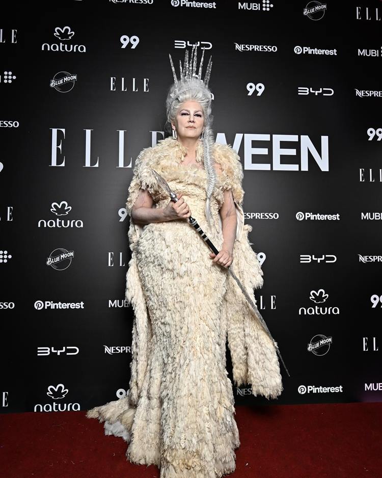 Susana Barbosao está vestida como a Rainha do Gelo para o Elleoween. Ela usa um vestido longo de textura felpuda, em tons de branco e gelo. Seu cabelo é branco, estilizado em um penteado alto com uma coroa de gelo. Maquiagem pálida e um cetro prateado completam o visual majestoso e frio.