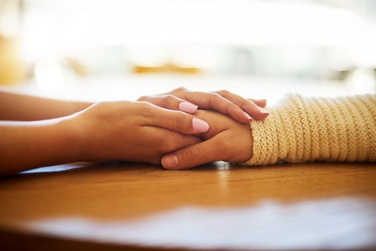 A imagem mostra duas mãos se tocando em um gesto de apoio e conforto sobre uma mesa de madeira. Esse símbolo de conexão humana reflete a essência da terapia, enquanto a inteligência artificial potencializa o alcance desse cuidado, oferecendo suporte emocional acessível e contínuo, mesmo à distância.