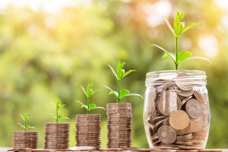 A imagem mostra quatro pilhas crescentes de moedas, cada uma com uma pequena planta brotando no topo, simbolizando crescimento. Ao lado, um pote cheio de moedas também tem uma planta. A cena representa a ideia de investir, destacando como o dinheiro pode crescer com o tempo, semelhante a jogar na loteria, mas com um foco em resultados sustentáveis.