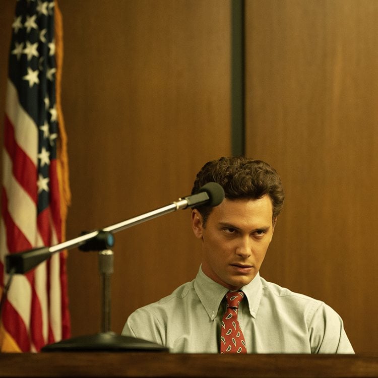 Foto de ator Cooper Koch interpretando Erik, sentado no tribunal usando camisa branca 