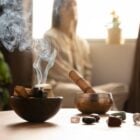 Foto de mesa com cristais e incenso e mulher de pele clara sentada meditando ao fundo desfocado