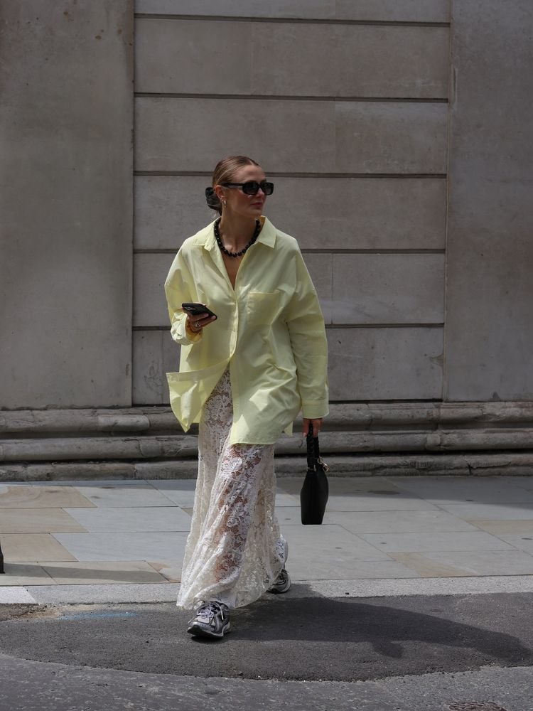 Mulher de pele clara usando camisa oversized amarelo manteiga e saia de renda branca