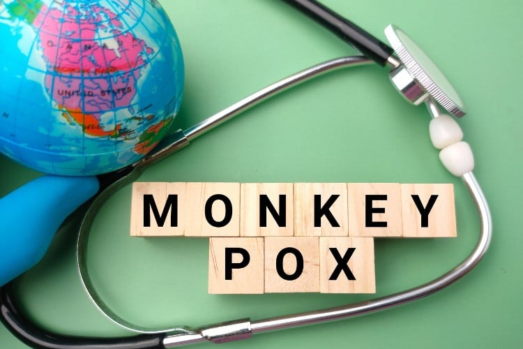 Foto de fundo verde com globo terrestre, estetoscópio e "Monkey pox" escrito com peças de palavra cruzada