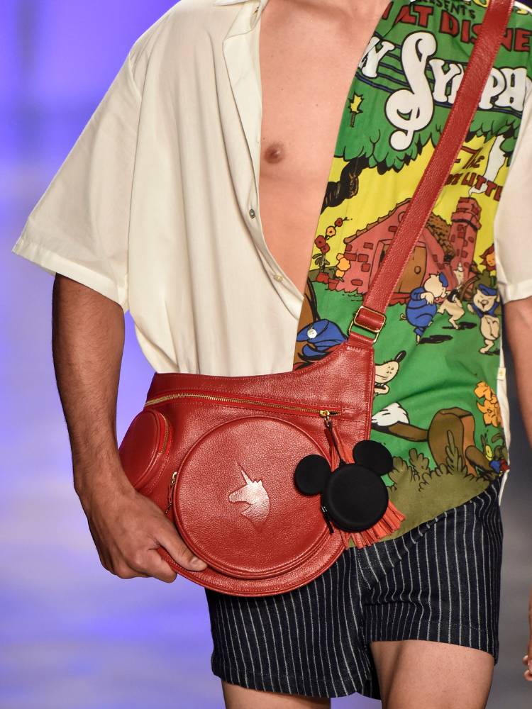 Zoom em homem com camisa dos Três Porquinhos e bolsa vermelha do Mickey