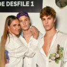 Fernanda Lima abraçada com um dos filhos e o outro gêmeo ao lado. Os três usam camisa branca com estampa da Disney para desfile da The Paradise na SPFW