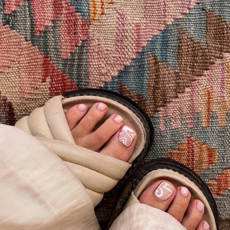 unhas decoradas de branco em sandália sob tapete