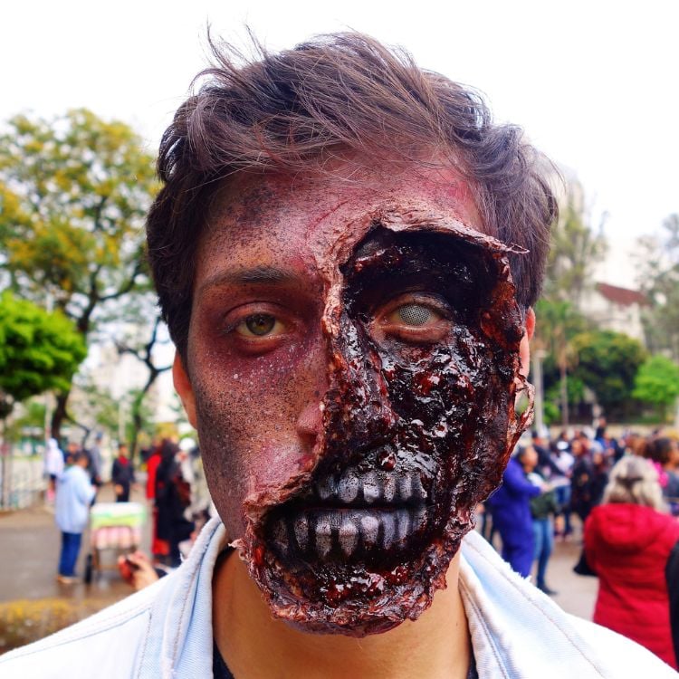 Homem de pele clara com maquiagem de zumbi com sangue falso e "músculos" faciais aparecendo 