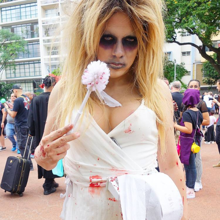 Mulher de pele clara com vestido branco manchado de sangue e maquiagem de zumbi 