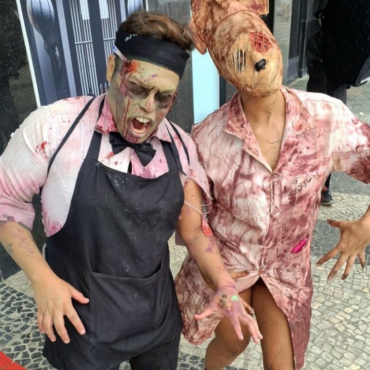 Homem fantasiado de zumbi verde com avental preto e mulher fantasiada de enfermeira de Silent Hill