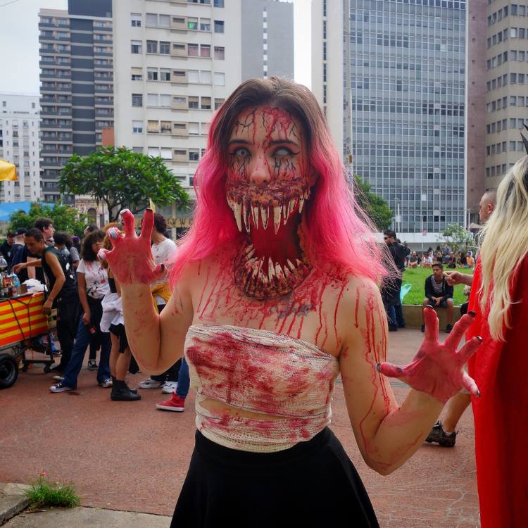 Mulher de pele clara usando blusa manchada de sangue falso, saia preta e maquiagem zumbi 