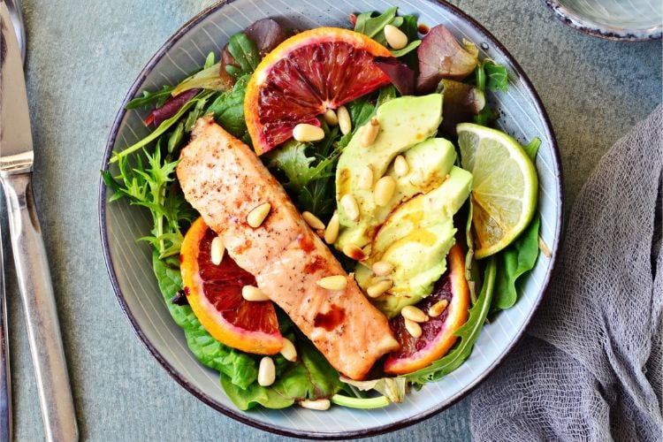 Foto de tigela com salada de folhas, abacate, salmão. limão e castanhas 