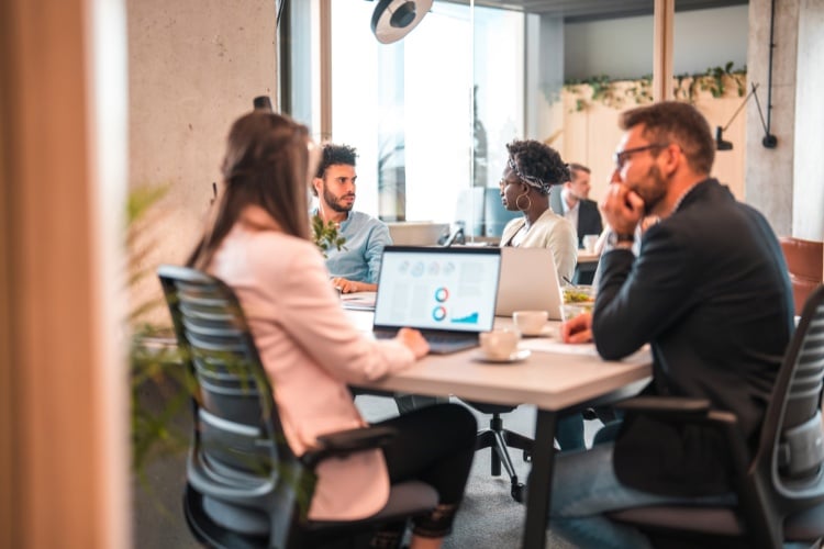 Reunião com pessoas sentadas ao redor de uma mesa vendo métricas no computador