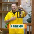 Um participante de A Fazenda 16 segura o Lampião, símbolo de poder no reality show. Ele veste uma camisa amarela e está em um cenário de pedras, expressando entusiasmo. O logotipo do programa, "A Fazenda", aparece em destaque na imagem.