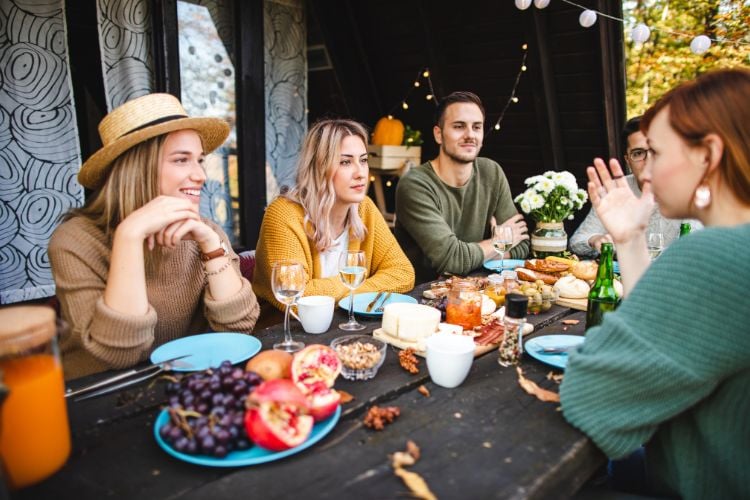 Homem e mulheres de pele clara conversando à mesa com comidas de brunch, como frutas e pães