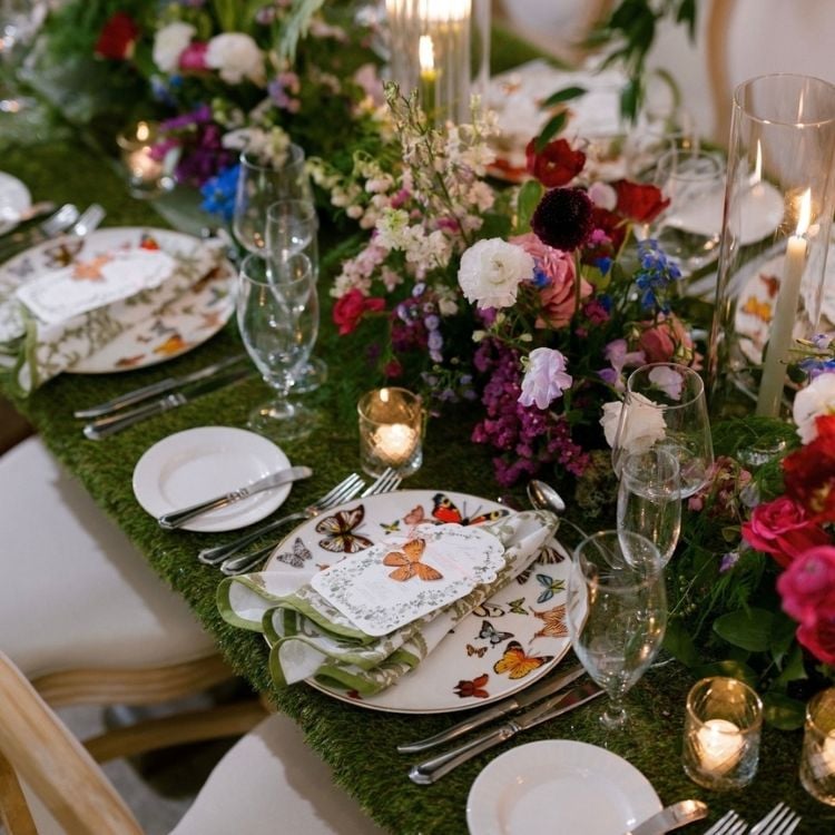 Mesa posta com pratos de borboletas, porta guardanapo de borboleta, guardanapo de tecido, velas e flores coloridas