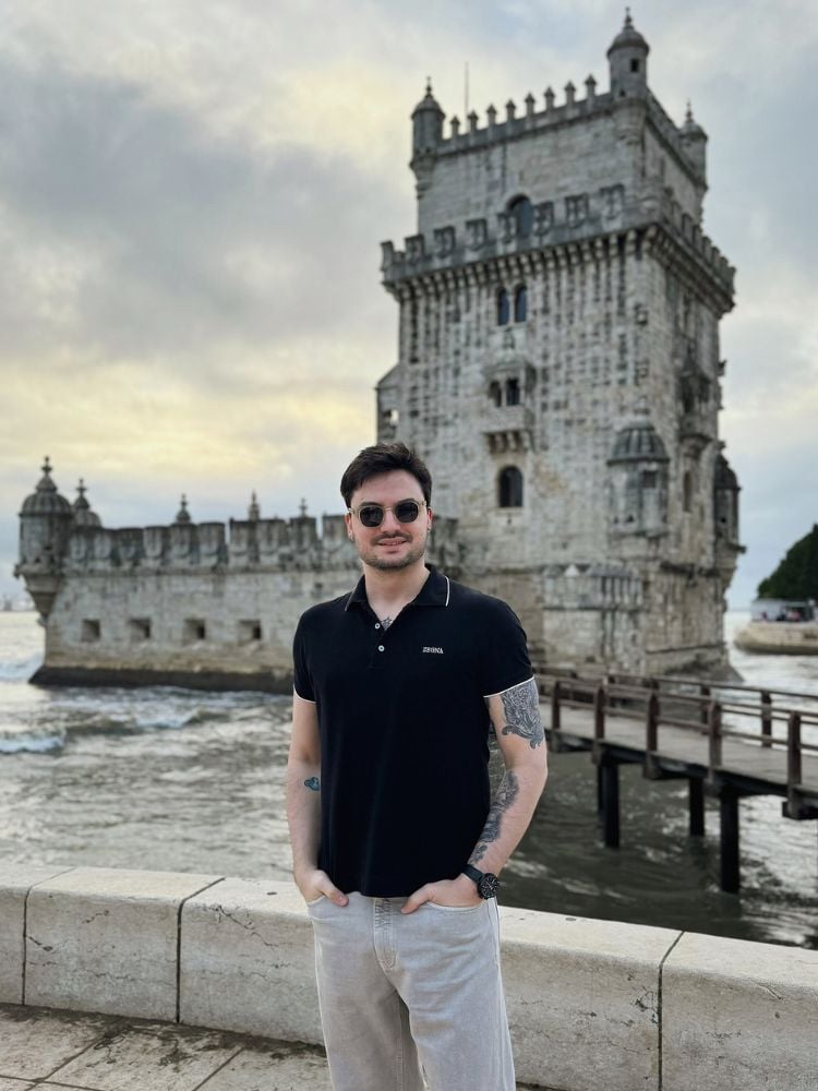 Foto de Felipe Neto usando camiseta preta e calça bege com castelo português ao fundo