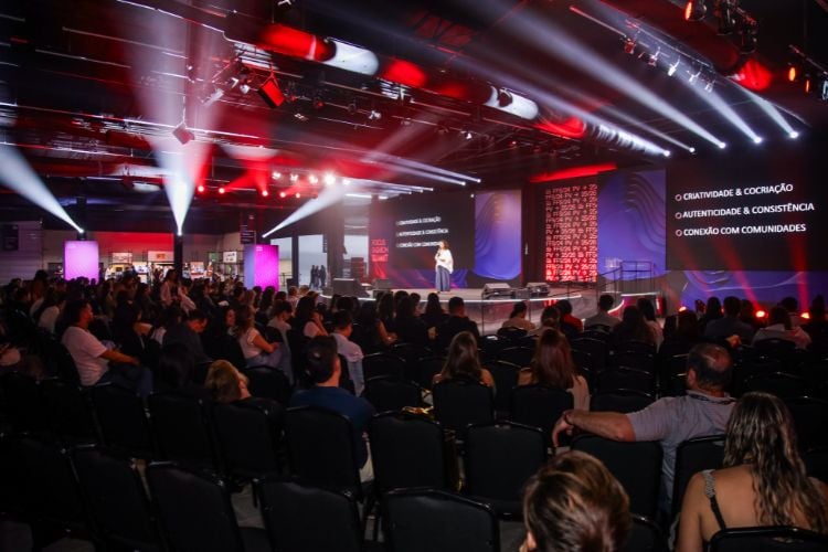 Foto de mulher de pele clara usando roupa branca e azul palestrando no palco do Focus Fashion Summit 