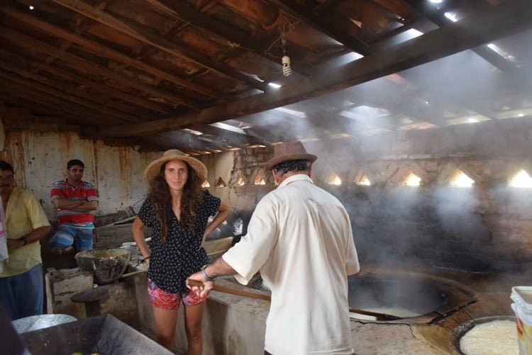 Influenciadora  Júlia Tolezano com chapéu de palha, em casa rústica, ao lado de outras pessoas cozinhando algo 